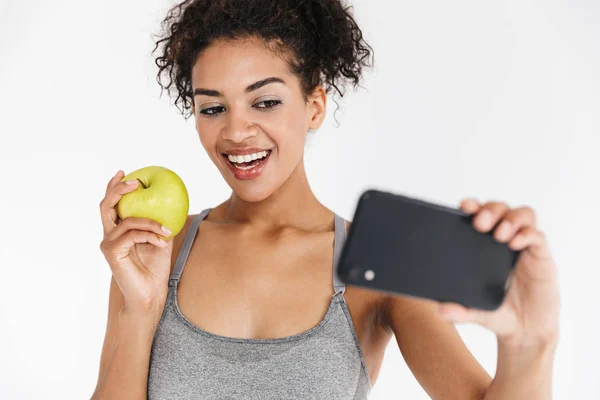 Beautful joven increíble deporte fitness africana mujer posando tomar selfie con manzana por teléfono móvil . —  Fotos de Stock