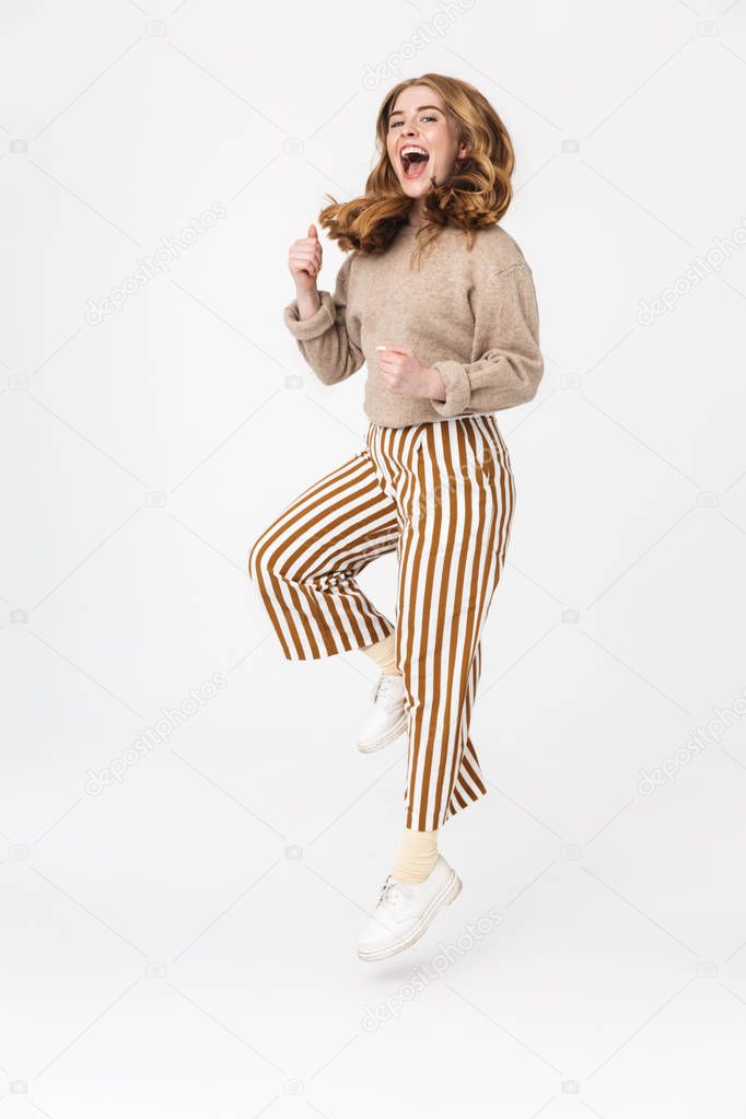 Excited cute young teenage girl posing isolated over white wall background make winner gesture.