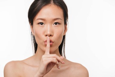 Ciddi genç güzel asya kadın sessizlik jest gösteren beyaz duvar arka plan üzerinde izole poz.