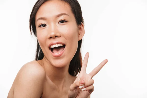 Heureux gai jeune belle asiatique femme posant isolé sur fond de mur blanc montrant geste de paix . — Photo