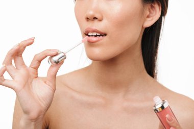 Güzel asya kadın makyaj ruj dudak parlatıcı tutarak beyaz duvar arka plan üzerinde izole poz.