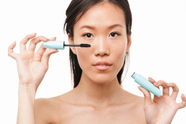 Güzel asyalı kadın makyaj maskara tutarak beyaz duvar arka plan üzerinde izole poz.