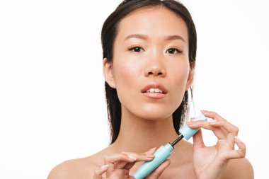 Güzel asyalı kadın makyaj maskara tutarak beyaz duvar arka plan üzerinde izole poz.