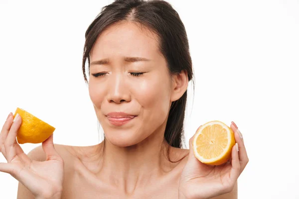 白い壁の背景の上に孤立したポーズの混乱した美しいアジアの女性はレモン柑橘類を食べる. — ストック写真