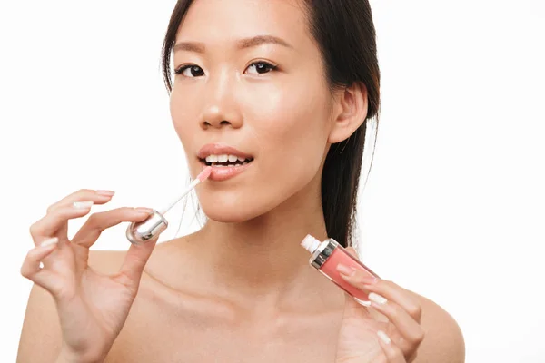 Hermosa mujer asiática posando aislada sobre fondo de pared blanca sosteniendo maquillaje lápiz labial brillo labial . — Foto de Stock