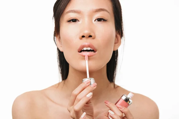 Hermosa mujer asiática posando aislada sobre fondo de pared blanca sosteniendo maquillaje lápiz labial brillo labial . — Foto de Stock