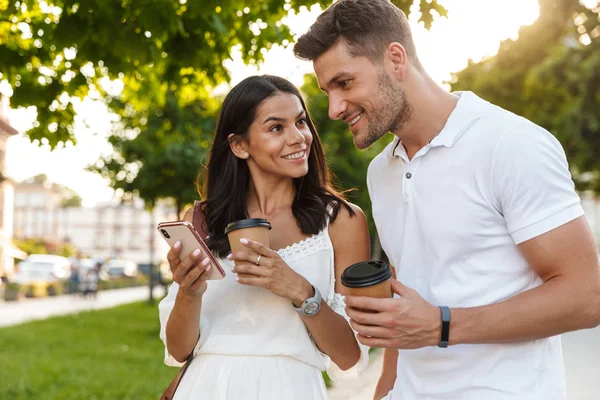 Porträt eines brünetten jungen Paares mit Smartphone beim Gehen — Stockfoto