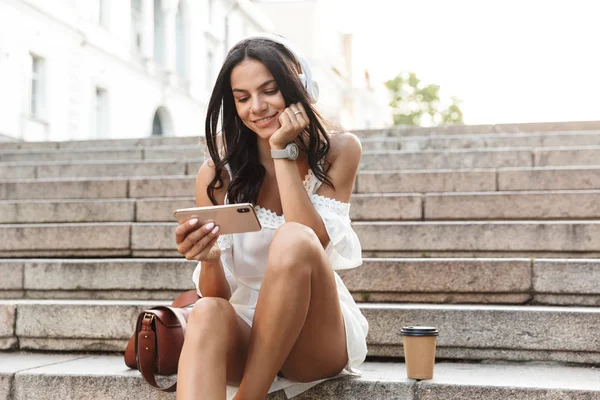 Retrato de encantadora jovem mulher usando fones de ouvido segurando smar — Fotografia de Stock