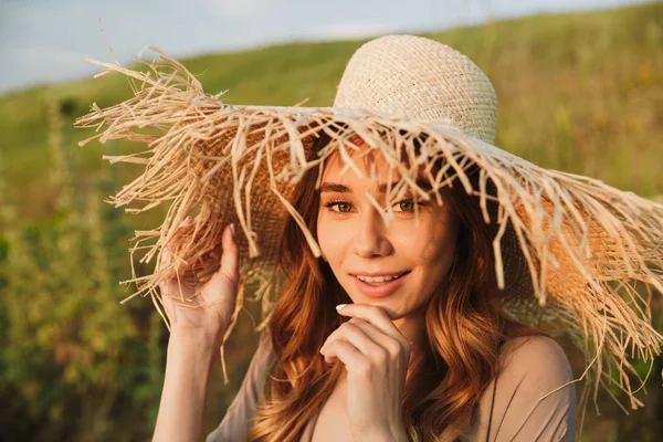 Gelukkig jonge mooie vrouw in hoed poseren buitenshuis op de natuur groen gras in de buurt van het strand. — Stockfoto