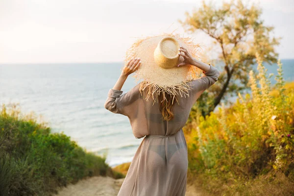 Joven bonita mujer en sombrero posando al aire libre en la naturaleza hierba verde cerca del mar de playa . — Foto de Stock