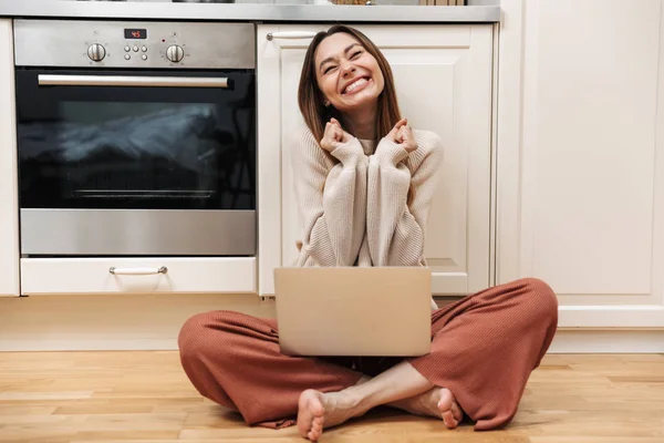 Fröhliches junges Mädchen sitzt auf einem Fußboden in der Küche — Stockfoto