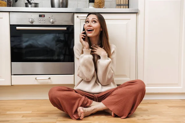 Cheerful young girl sitting on a floor at the kitchen — Stock Photo, Image