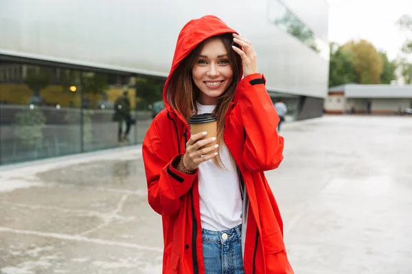 Güzel heyecanlı duygusal genç mutlu güzel kadın yağmurluk açık havada kahve içme poz. — Stok fotoğraf