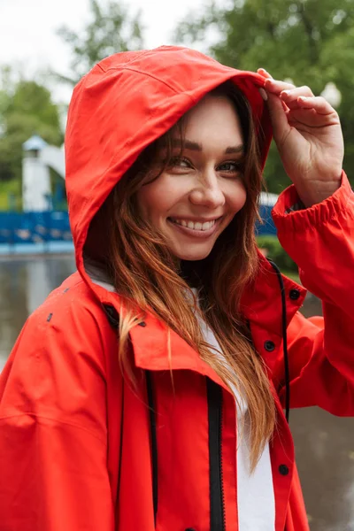 Imagem da jovem mulher alegre 20s em capa de chuva colorida andando thr — Fotografia de Stock