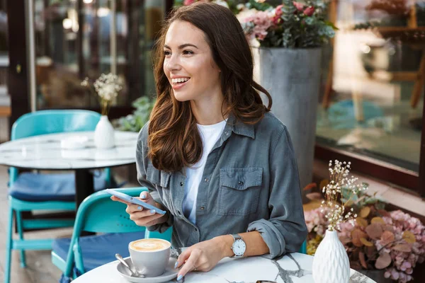 Piękna młoda dziewczyna siedzi w kawiarni na świeżym powietrzu — Zdjęcie stockowe