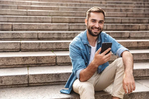 Smiling young man sitting on stairs outdoors — Stock Photo, Image