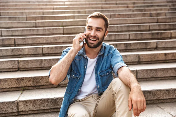 Smiling young man sitting on stairs outdoors — Stock Photo, Image