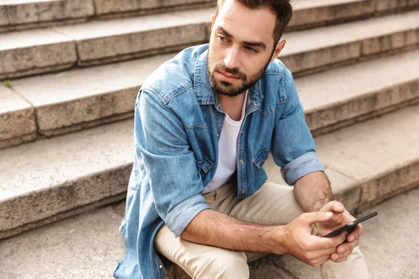 Açık havada merdivenlerde oturan gülümseyen genç adam