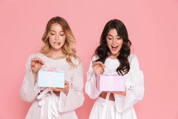 Gelukkig jonge twee mooie vrouwen meisjes vrienden zusters poseren geïsoleerd over roze muur achtergrond houden huidige vakken. — Stockfoto