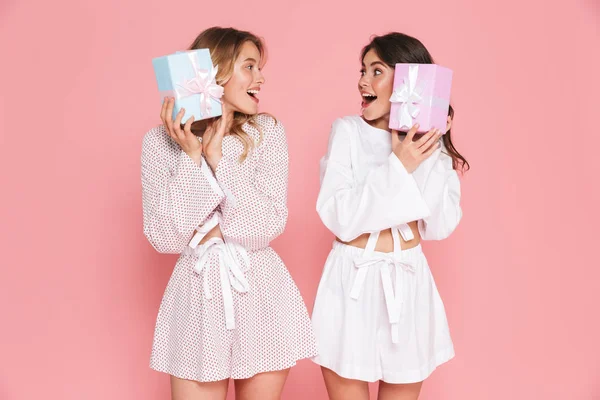 Gelukkig jonge twee mooie vrouwen meisjes vrienden zusters poseren geïsoleerd over roze muur achtergrond houden huidige vakken. — Stockfoto