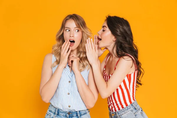 Retrato de dos mujeres caucásicas rubias y morenas de 20 años en ropa de verano expresando sorpresa mientras susurran chismes — Foto de Stock