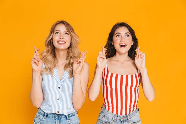 Portret dwóch szczęśliwych blond i Brunette kobiet 20s w lecie nosić Dreaming przy jednoczesnym zachowaniu kciuki — Zdjęcie stockowe