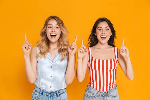 Retrato de dos mujeres rubias y morenas positivas de 20 años en verano llevan sonriendo mientras señalan con los dedos al copyspace —  Fotos de Stock