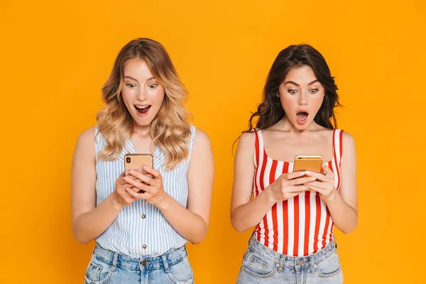 Retrato de dos mujeres excitadas rubias y morenas de 20 años en verano llevan sonriendo mientras sostienen teléfonos celulares — Foto de Stock
