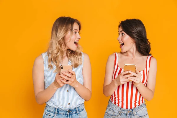 Retrato de dos mujeres rubias y morenas encantadas de 20 años en verano llevan sonriendo mientras sostienen teléfonos celulares — Foto de Stock