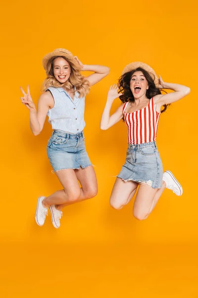 Портрет двух счастливых блондинок и брюнеток 20 лет в соломенных шляпах в знак мира поют и прыгают — стоковое фото