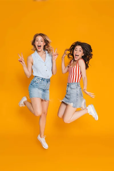 Ritratto di due donne bionde e brune stupite di 20 anni in gonne di denim che gesticolano la pace cantano e saltano — Foto Stock