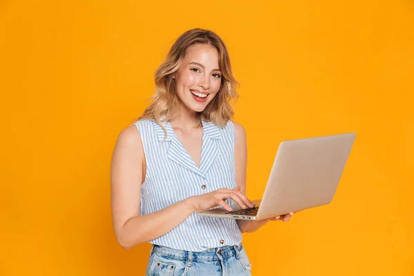 Portrait of nice blonde woman in casual clothes smiling at camera while typing on laptop — Stock Photo, Image