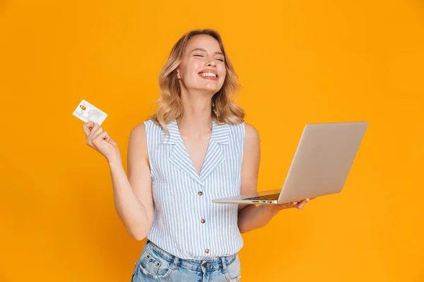 Portrait de sourire femme heureuse en vêtements décontractés tenant carte de crédit et ordinateur portable avec les yeux fermés — Photo