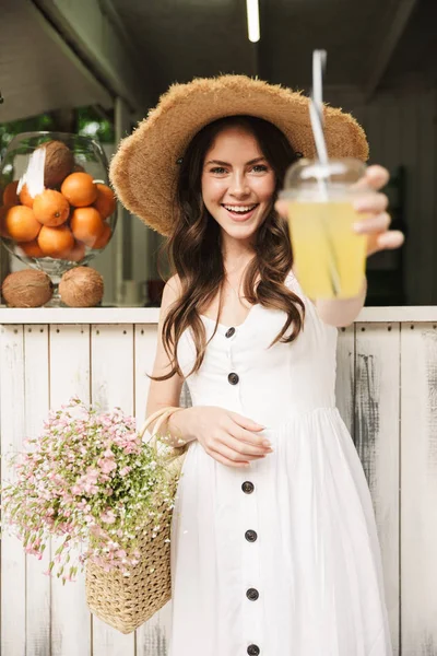 Cheerful happy young pretty woman outoors in park posing in hat holding juice. — Stock Photo, Image