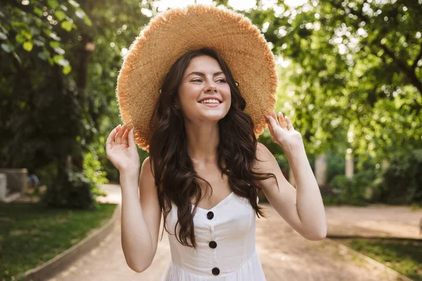 Těší mě šťastná Mladá hezká ženská, když chodí v klobouku do zeleného parku. — Stock fotografie