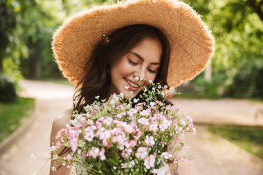 Yeşil parkta çiçekler tutan şapka yürüyüş Heyecanlı mutlu genç güzel kadın outoors.