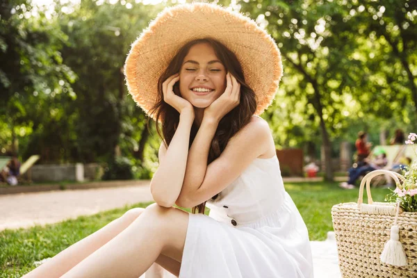 Jovem feliz mulher bonita outoors no parque verde em chapéu sentado na grama . — Fotografia de Stock