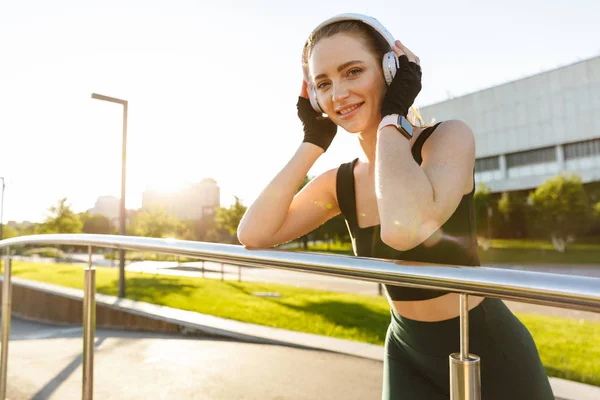 Image of feminine fitness woman leaning on railing and listening