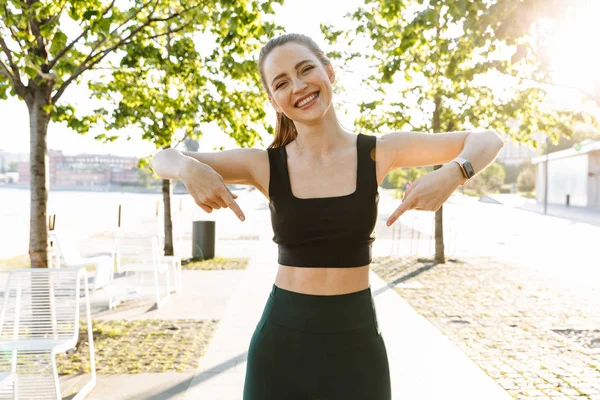 Image of athletic sportswoman smiling and pointing fingers at he — Stock Photo, Image