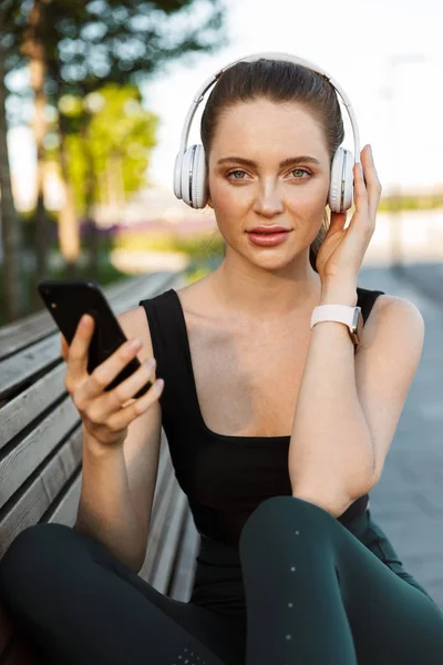 Immagine di sportiva femminile che tiene smartphone e ascolta — Foto Stock