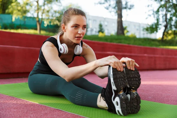 Foto de una joven deportista estirando su cuerpo en la colchoneta de fitness d — Foto de Stock