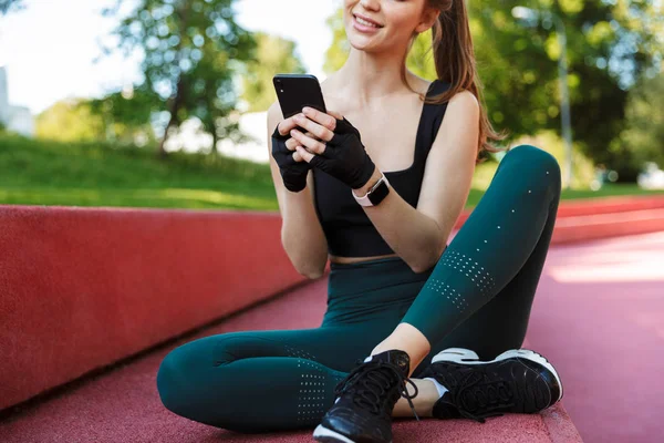 Photo of joyful young woman holding smartphone while sitting on — Stock Photo, Image