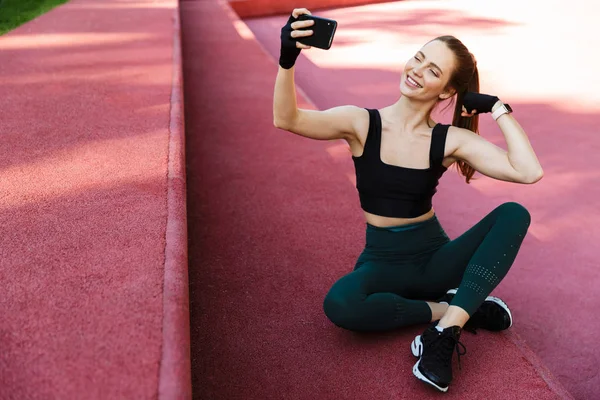 Foto de la mujer joven de fitness tomando selfie en el teléfono inteligente mientras s — Foto de Stock
