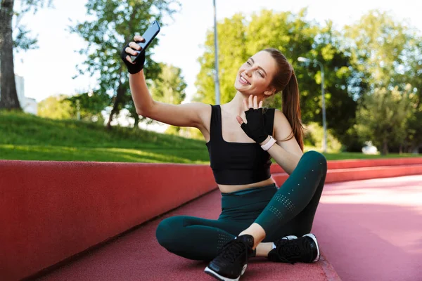 Foto de la joven alegre tomando selfie en el teléfono inteligente mientras si —  Fotos de Stock