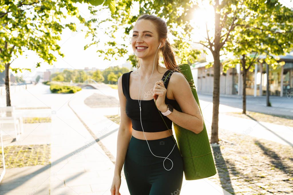 Image of slim sportswoman listening to music with earphones and 