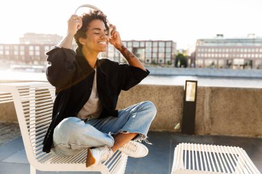 Nehir kenarındaki bankta otururken kulaklık kullanan güzel Afro-Amerikan kadının portre yakın çekim