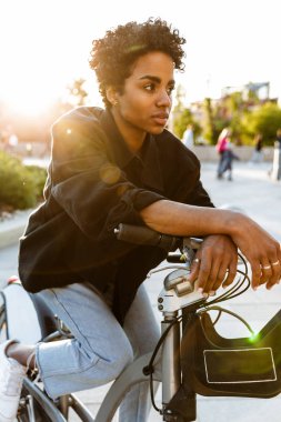 Şehir parkında bisiklet üzerinde otururken kenara bakan ciddi afro-amerikan kadın fotoğrafı