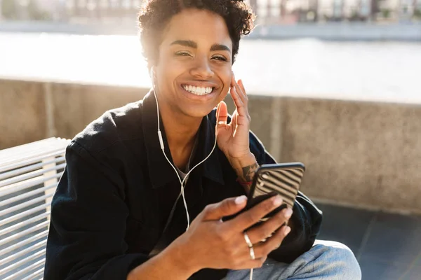 Nehir kenarında kulaklıkla cep telefonundan müzik dinleyen afro-amerikan kadının portre yakın çekimi — Stok fotoğraf