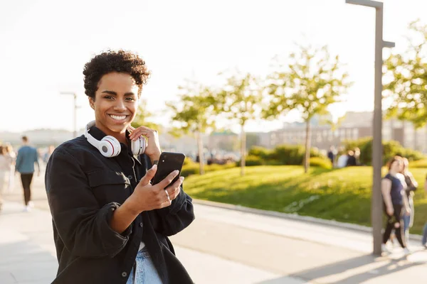Porträtt närbild av leende afrikansk amerikansk kvinna med mobiltelefon och leende medan du går på City Street — Stockfoto