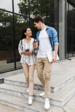 Şehir caddesinde gezinirken paket kahve içen sevimli çiftin görüntüsü